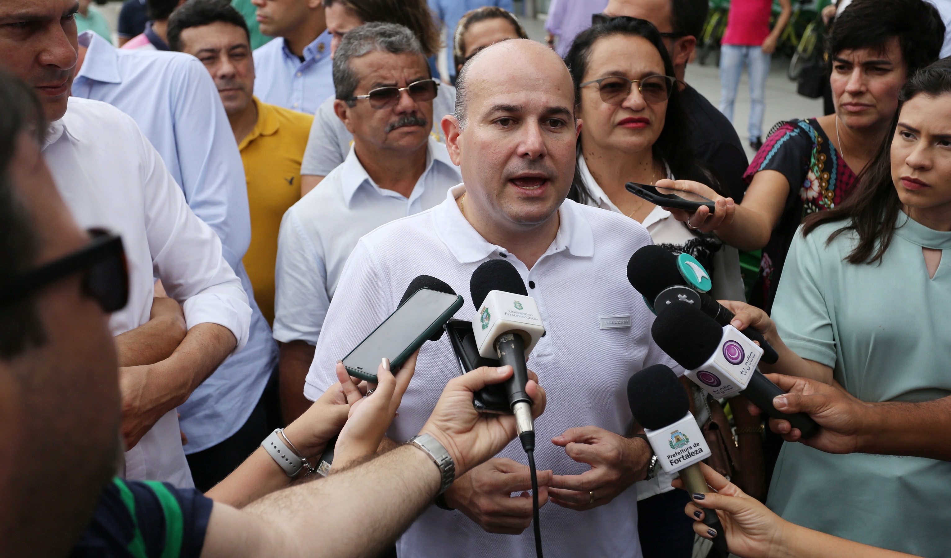 prefeito dando entrevista para vários jornalistas segurando microfones e gravadores